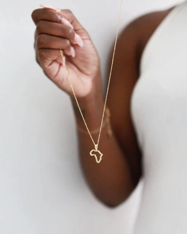 Gold necklace with a heart pendant held by a hand against a white background
