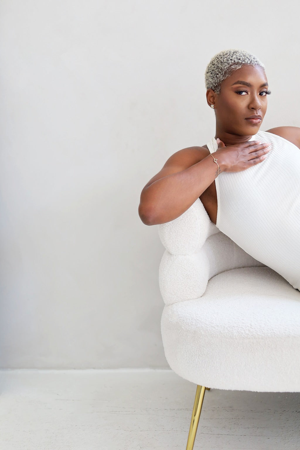 Woman sitting on a white chair holding a white pillow against a plain background