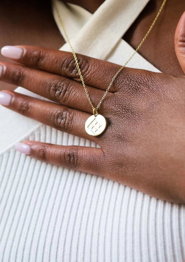 Gold necklace with a round pendant on a hand against a neutral background