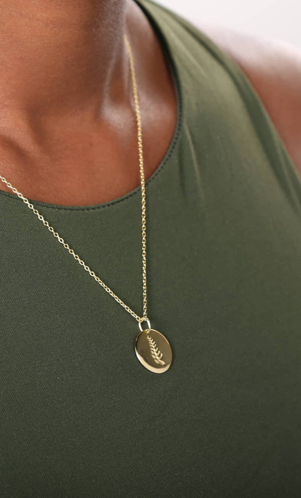Gold necklace with a pendant on a person wearing a green top.
